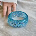 Close-up of a vibrant blue resin bangle bracelet with shimmering iridescent flakes - Blue