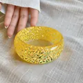 Detail shot of a vibrant yellow resin bangle with shimmering holographic glitter inside. - Yellow