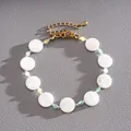 Close-up of elegant gold bracelet with circular white shell beads and colored glass accents - White
