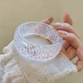 Detail view of a clear resin bangle with shimmering iridescent flakes held by hand. - White
