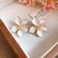 Close-up of white enamel flower stud earrings with golden edges on a wooden tray - Tops / White