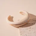 Close-up shot of a beige acrylic wave bangle featuring an elegant marbled ink-wash pattern. - White
