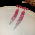 Close-up of pink rhinestone bow tassel earrings with sparkling details on white tray. - Pink
