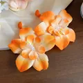 Close-up shot of vibrant orange fabric flower stud earrings with raffia detail accents - Stud Earrings / Orange