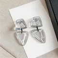 Detalle de pendientes colgantes geométricos de resina gris con pines de plata en tarjeta - Geométrico / Blanco