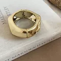 Close-up of a chunky gold irregular geometric bangle on an artistic book background - Gold