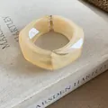 Dettaglio di un ampio bracciale rigido in resina crema irregolare su un libro aperto - Giallo