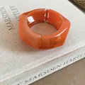 Macro detail of a stylish chunky orange irregular resin hinge bangle on a fabric art book - Orange