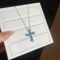 Nahaufnahme einer silberfarbenen Halskette mit einem blau-weißen Zirkon-Kreuzanhänger. - Groß