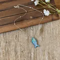 Detailed view of an iridescent blue fish pendant necklace on a rustic burlap surface - Iridescent Fish Choker