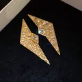 Close-up view of geometric gold-plated earrings with zircon inlays on dark velvet - Gold