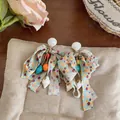 Detailed macro view of chiffon bow earrings with shell and conch pendants for beach style - Conch Style / Colorful
