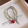 Detalle macro de una pulsera de perlas multicapa con lazo de circón y dije de manzana - Estilo de Manzana con Lazo de Perlas de Capas / Blanco y Rojo