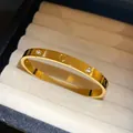 Macro view of gold stainless steel buckle bangle featuring heart engraving and zircons - Heart and Round Stone Style / Gold