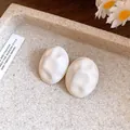 Close-up of minimalist white oval earrings with a crumpled texture on a stone tray. - Beige
