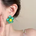 Close-up detail of a colorful green and yellow flower stud earring worn on an Asian model - Hollow Flower / Green-Yellow