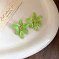 Vue détaillée de boucles d'oreilles fleurs en émail vert avec bordure dorée sur plateau - Vert