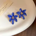 Gros plan de boucles d'oreilles fleur en émail bleu avec centre doré sur assiette - Bleu