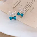 Dettaglio macro di orecchini a fiocco con cuore blu ghiaccio e accenti di perle. - Stile Fiocco Cuore (HE34141) / Blu
