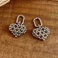 Detail of silver beaded heart charm earrings on a rustic wooden background. - Silver