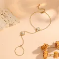 Detailed view of gold stainless steel hand chain with white flower charms on beige background - White Shell Flower Hand Chain (O711) / Gold