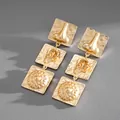Detailed view of gold-tone tiered square earrings featuring unique anatomical relief patterns. - Gold