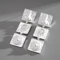 Close-up of avant-garde silver square drop earrings with 3D anatomical relief patterns - Silver