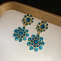 Close-up of vintage gold-tone earrings featuring sparkling blue sunburst rhinestones. - Earrings / Blue