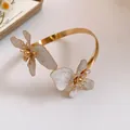 Nahaufnahme eines goldenen Armreifs mit eleganten weiß marmorierten Emaille-Blütenblättern - Weiß