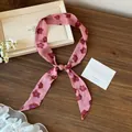 Elegante bufanda de seda rosa con flores presentada sobre fondo de madera rústica. - Estampado Floral / Rosa