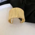 Dettaglio macro di un bracciale a fascia rigida dorato con filo avvolto su base chiara. - Stile 21 - Oro