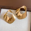 Detailed view of large gold hollow geometric earrings with a hammered twisted metal texture - Gold