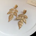 Elegante vista ravvicinata di orecchini a forma di foglia dorata con trama in metallo pieghettato - Oro