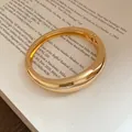 Primo piano di un bracciale rigido dorato lucido posato su pagine di un libro - Stile 5
