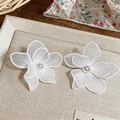 Elegant white mesh flower earrings with pearl centers on a textured display tray. - Flower Style / White