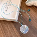 Detail view of coastal blue cord necklace featuring a round seashell and pearl pendant - Round Style with Glass Fragments / Blue