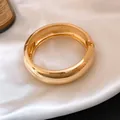 Macro view of a polished gold chunky metal bangle with hinge on luxury white satin - Thickened Round Mirror Style / Gold