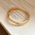 Close-up of a golden metal wrinkled bangle bracelet with elegant twisted design - Irregular Wide Pleated Style / Gold