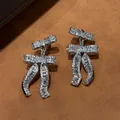 Sparkling silver bowtie dangle earrings featuring 18k gold plating and clear zircons. - Silver