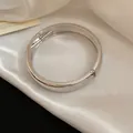 Detailed close-up of a polished silver metal hinged bangle on white satin fabric - Minimalist Rounded Polished Style / Silver
