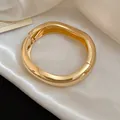 Macro view of a luxurious gold-tone wavy chunky metal bangle on white silk fabric - Irregular Wavy Pleated Style / Gold