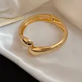 Close-up of an elegant gold pleated metal bangle with polished finish on white silk - Twisted Teardrop Pleated Style / Gold