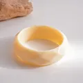 Nahaufnahme eines cremefarbenen Acryl-Armreifs mit facettiertem geometrischem Design - Weiß
