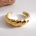 Detailaufnahme eines klobigen, goldenen, gedrehten Armreifs mit hochglanzpoliertem Finish - Gold