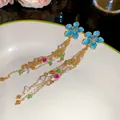 Close-up view of blue enamel flower earrings with long gold chain tassels and beads - Blue Flower Tassel (HE34240) / Silver Needle / Gold