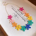 Close-up detail of colorful raffia flower charms on a bohemian style gold chain necklace - Necklace / Gold-Multicolor