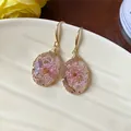 Close-up of elegant resin teardrop earrings with pink dried flowers and gold hooks. - Gold-Pink