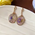 Detail shot of teardrop resin earrings featuring delicate real dried flowers inside. - Gold-Pink-Blue