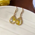 Close-up of teardrop resin earrings featuring delicate yellow dried flowers inside. - Hook Earring (HE31316) / Gold-Yellow