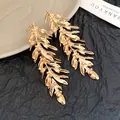 Detailed view of elegant gold leaf feather tassel earrings on textured black paper. - Silver Earring Post Style / Gold